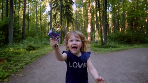 Happy Kid Blows Bubbles From Special Manual Bubble Machine Outdoors in Park alt