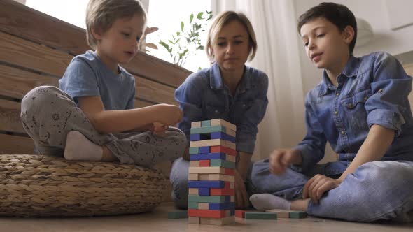 Two Boys Brothers Are Building a Tower From Wooden Blocks Sitting on the Floor alt