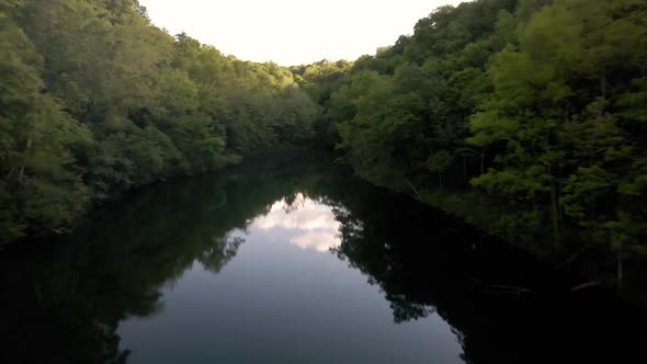 This is a aerial shot of a private lake with a little cabin on it surrounded by tons of forest. alt