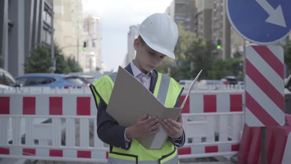Portrait Little Boy Wearing Safety Equipment and Constructor Helmet Reading Building Plan alt