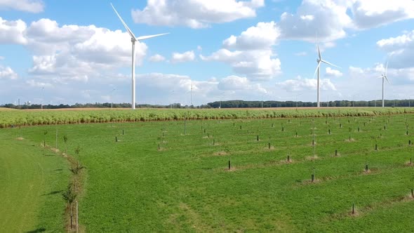 Drone rises over a  grass field filled with wind turbines on a fluffy cloud day. alt