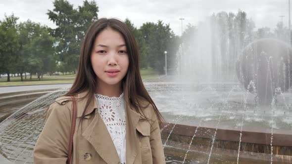 Girl Stands in the Background of the Fountain Looking at the Camera and Smiling