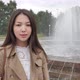 Girl Stands in the Background of the Fountain Looking at the Camera and Smiling - VideoHive Item for Sale
