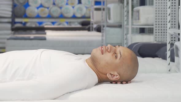 Happy African Man Lying on Orthopedic Mattress at Furniture Store