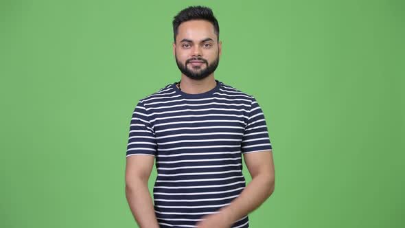 Young Happy Bearded Indian Man with Arms Crossed Against Green Background