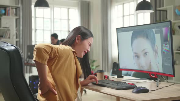 Asian Female Digital Editor Paining Her Back While Works In Photo Editing Software On Computer alt