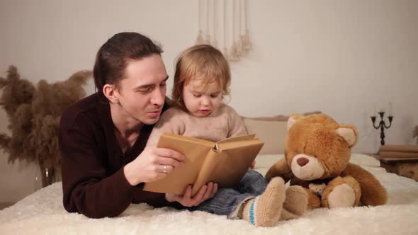 A Dad Reads His Daughter a Book on a Bed in the Room