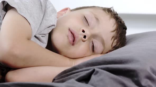Little preschool boy sleeping in his bed lying on his side. A boy in a gray T-shirt. alt