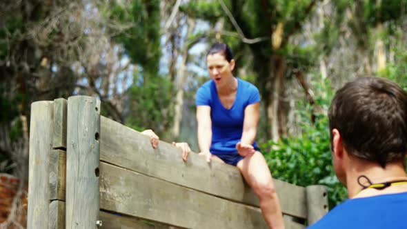 Female trainer assisting fit woman to climb over wooden wall during obstacle course 4k alt