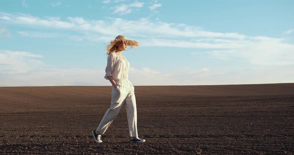Young Confident Woman is walking on Sunny Day on Field in Straw Hat.