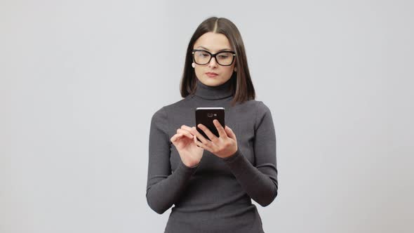 Woman In Glasses And Gray Turtle Neck Dress Scrolling Social Networks On Her Cell Phone