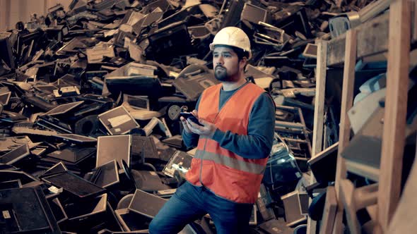 Dumpsite Worker with a Smartphone is Standing Near a Pile of Rubbish alt
