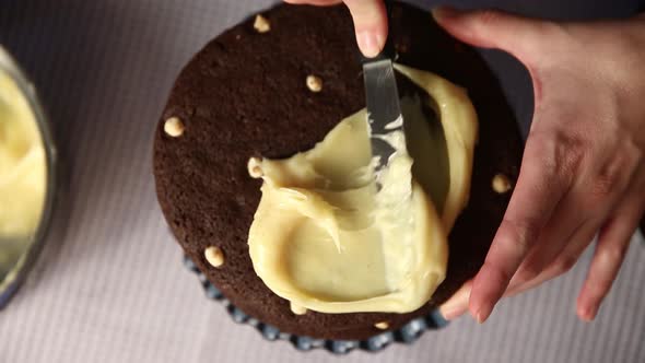 Spreading a cream filling between layers of a chocolate cake - top down view alt