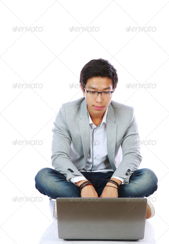 Young Asian Man Sitting On The Floor And Using Laptop Over White