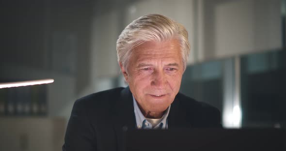 Professional Mature Businessman Sitting in Dark Office and Working on Laptop alt