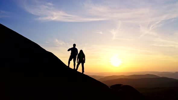 Silhouettes of Happy Men and Women Triumphantly Raising Their Hands Standing on the Rocky Ridge of