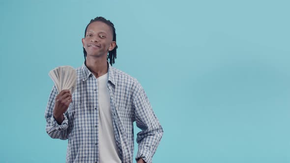 Black man with dreadlocks waves a bundle of dollar bills holding a fan in hand and staring alt