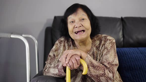 senior woman laughing and holding wooden cane in living room at home
