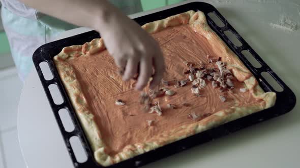 Woman smears sauce with brush on base for pizza on oven tray