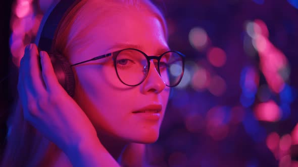 A Woman in Glasses and Headphones Against a Background of Colored Flickering Lights