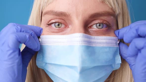 Close Up of 30s Female Doctor or Nurse Wear Blue Gloves Taking Off Face Mask to Breathe in Lab