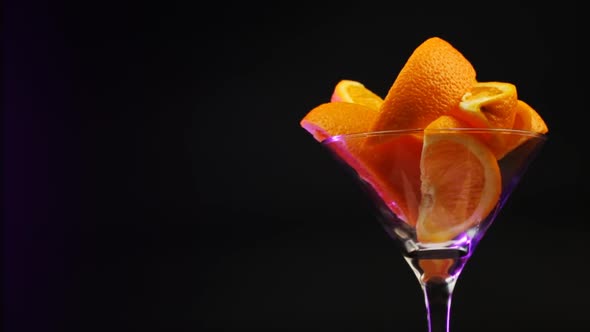 Oranges In A Martini Glass Rotate On A Black Background In A Purple Hue