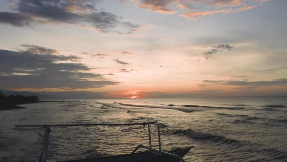 Aerial Shot of Silhouette of a Fishing Boat Floating on Sea Water with Waves Rolling on Beach alt