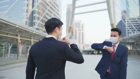 Asian business people wearing protective face mask making elbow touch  to avoid coronavirus in city. alt