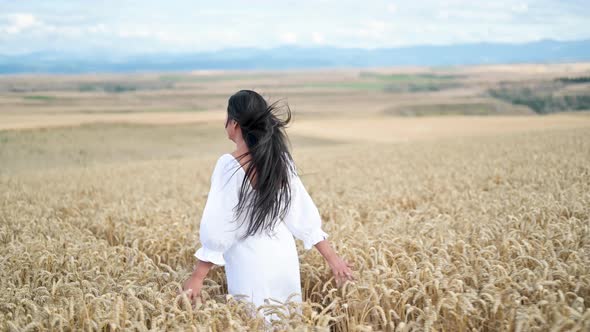 Young Hispanic Woman in White Dress Walking in the Middle of a Wheat Field Smiling at the Camera alt