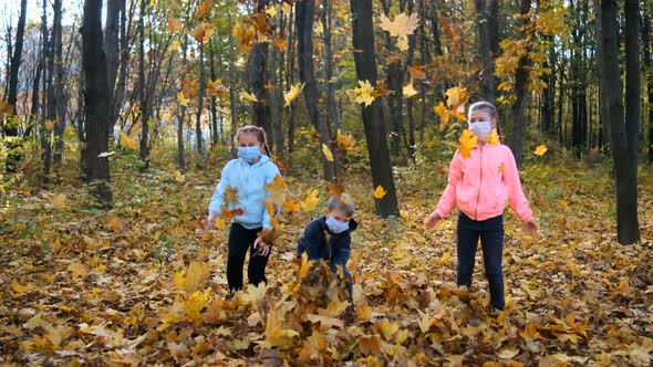 Small children in medical masks throw fallen yellow leaves in the Park on an autumn day. 