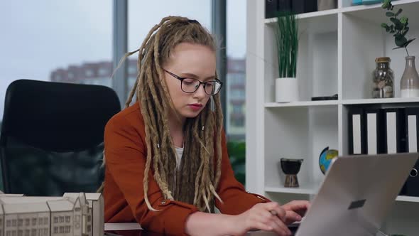 Female Engineer-Designer with Dreadlocks Working on Laptop in Modern Design Studio Agency alt