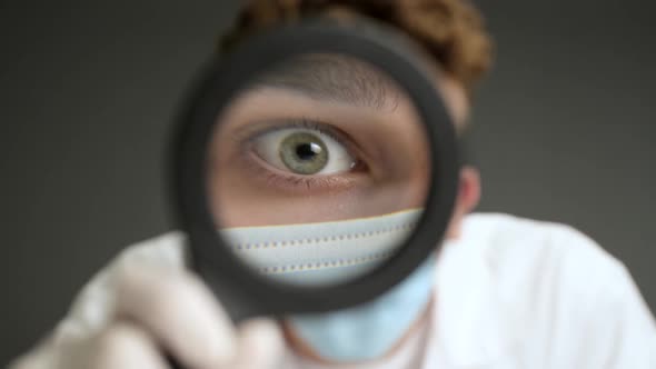 Student Intern in medical protection face mask is looking  through a magnifying glass