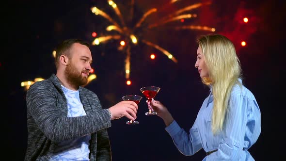 Happy Couple Loving Knocking Glasses Wine on Background Firework in Night Date. alt