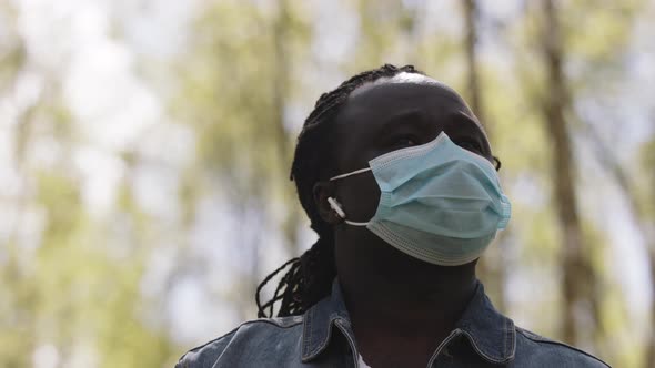 Portrait Shot of an African Man with Medical Mask and Wireless Headphones in the Nature alt