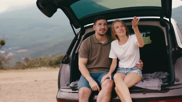 Young Traveler Couple on Road Trip in Mountains Sitting in a Trunk of a Car