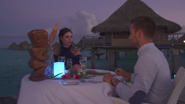 A man and woman couple dining on a deck pier at night in Bora Bora tropical island alt