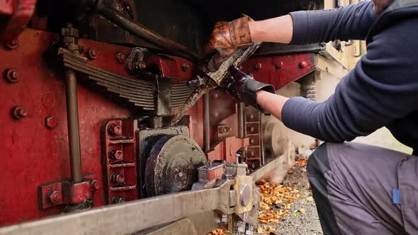 Mechanic adding oil in mechanisms of the stopped steam train Mocanita on a railway station in Romani alt