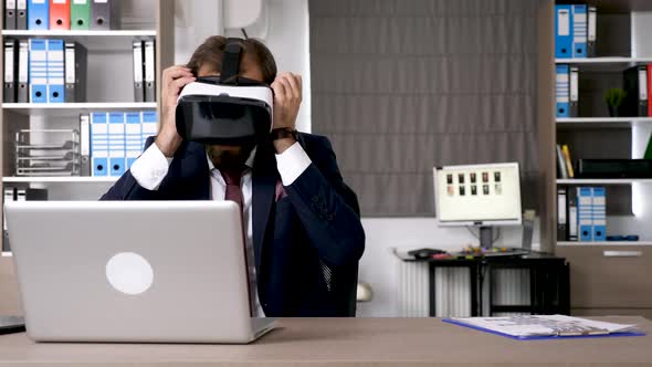 Businessman Works on the Computer Than Picks Up a VR Headset alt