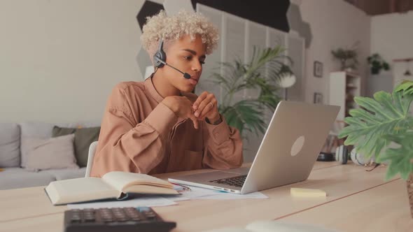 African Female Student Wearing Headset Looking at Laptop Watching Online Webinar alt