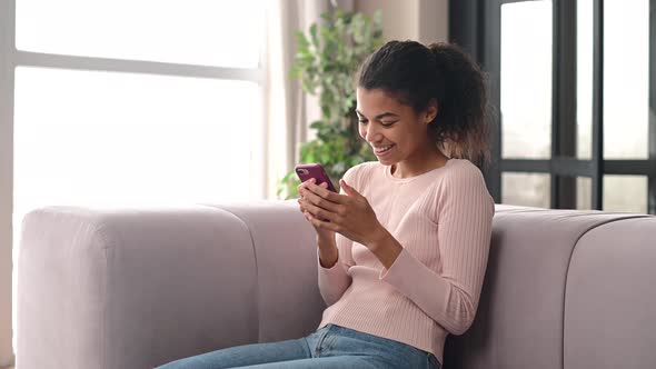 An Attractive Young AfricanAmerican Woman Using a Smartphone at Home alt