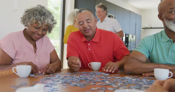 Happy senior diverse people playing puzzle at table at retirement home alt