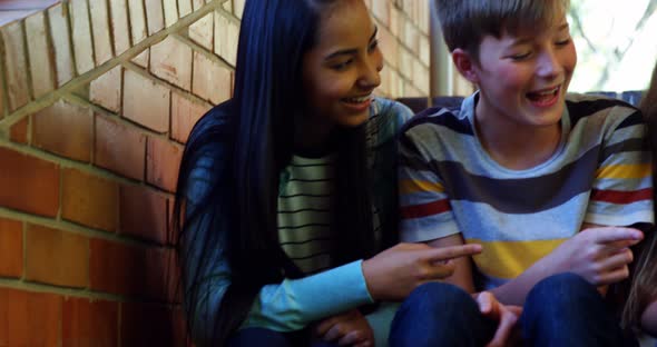 Smiling school students sitting on the staircase using mobile phone alt