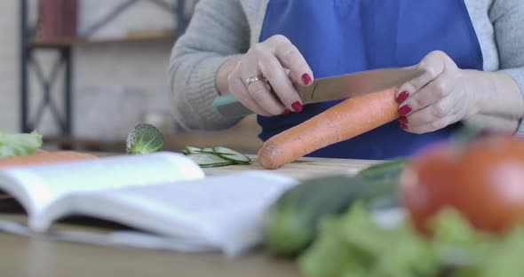 Middle-aged Female Caucasian Hand Peeling Carrot with Knife. Close-up of Senior Unrecognizable alt