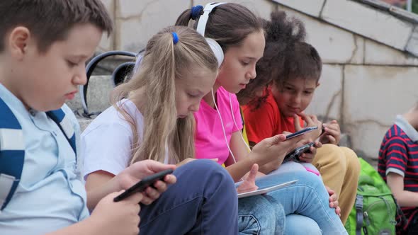 Schoolchildren Use Gadgets Resting on Steps After Lessons alt