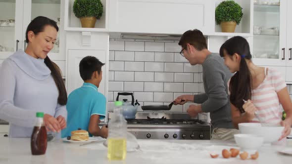 Happy asian parents in kitchen with son and daughter, father flipping pancake while they watch alt