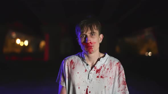 Psycho murderer at crime scene with blood splatter on clothes looks at camera. alt