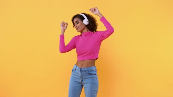 Happy fashionable African American woman listening to music on wireless headphones and dancing