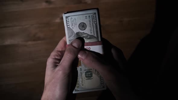 Male Hands Hold Three Stacks of 10000 US Dollar Bills on Wooden Background alt