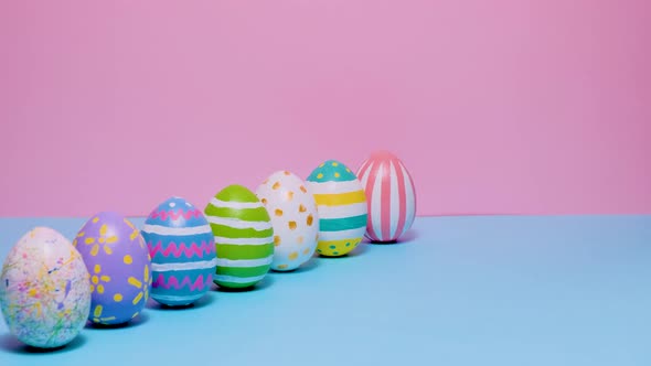 Colorful Painted Easter Eggs Roll and Knock Each Other on a Blue and Pink Background alt