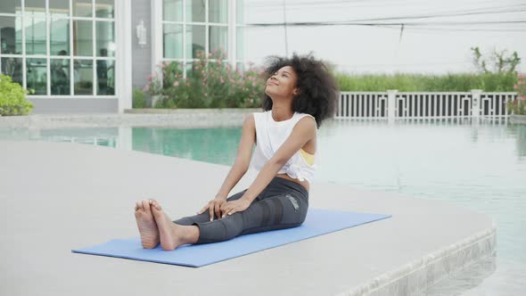Young African American woman doing exercise with stretch muscles lag in the poolside. alt